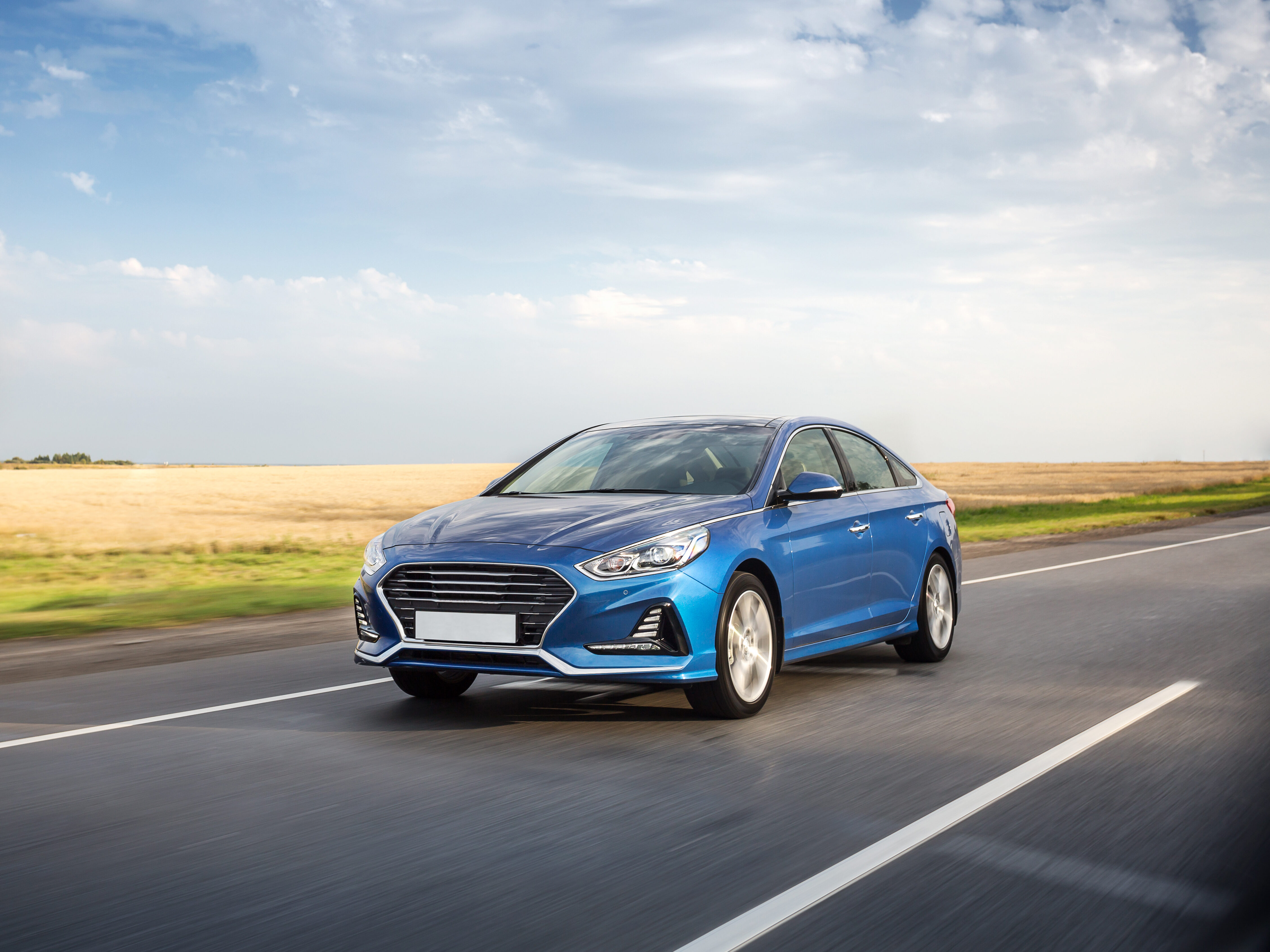 Blue car moving on th countryside road throught the yellow fields